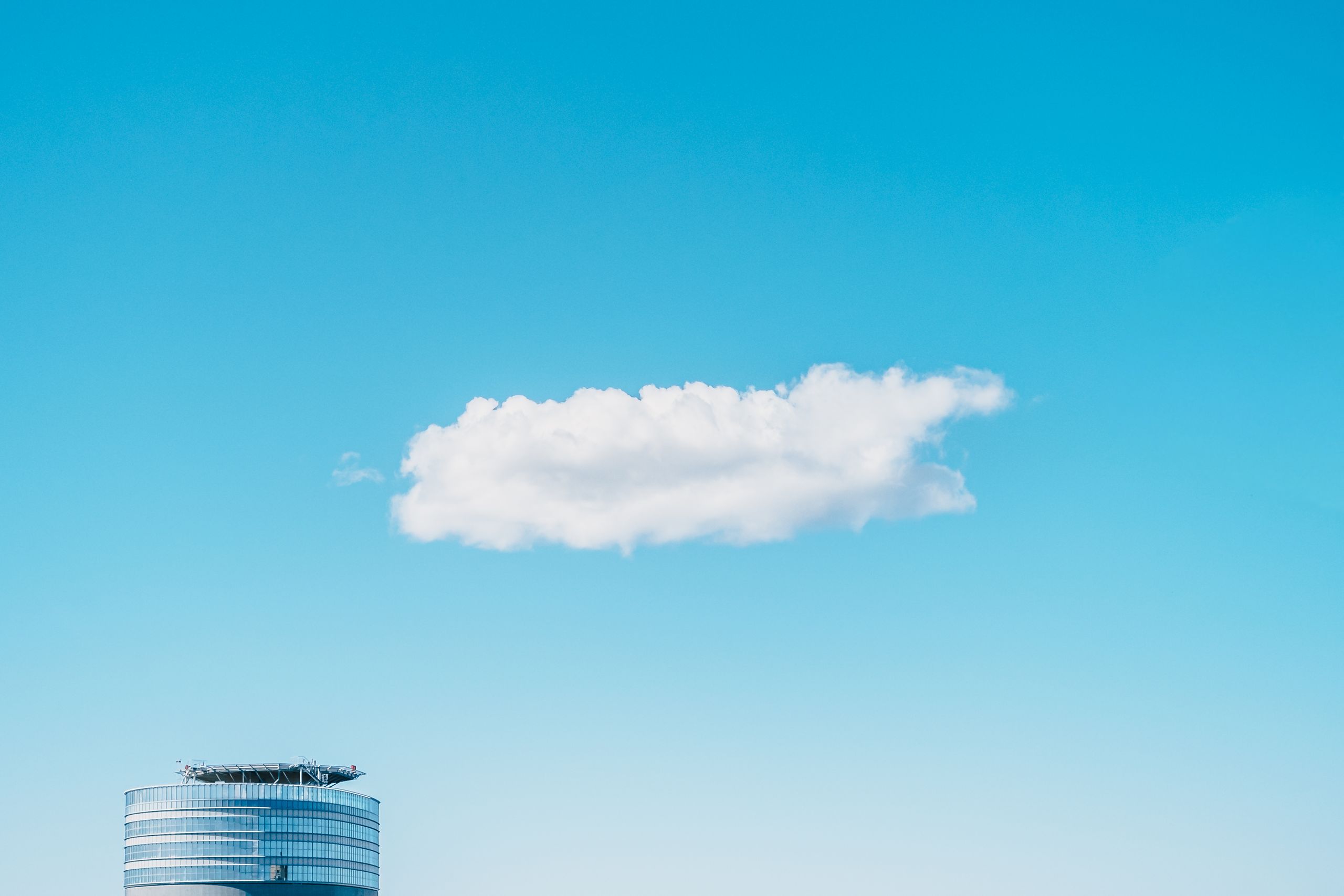 From below of lonely cloud floating in blue sky over high rise skyscraper in sunny day