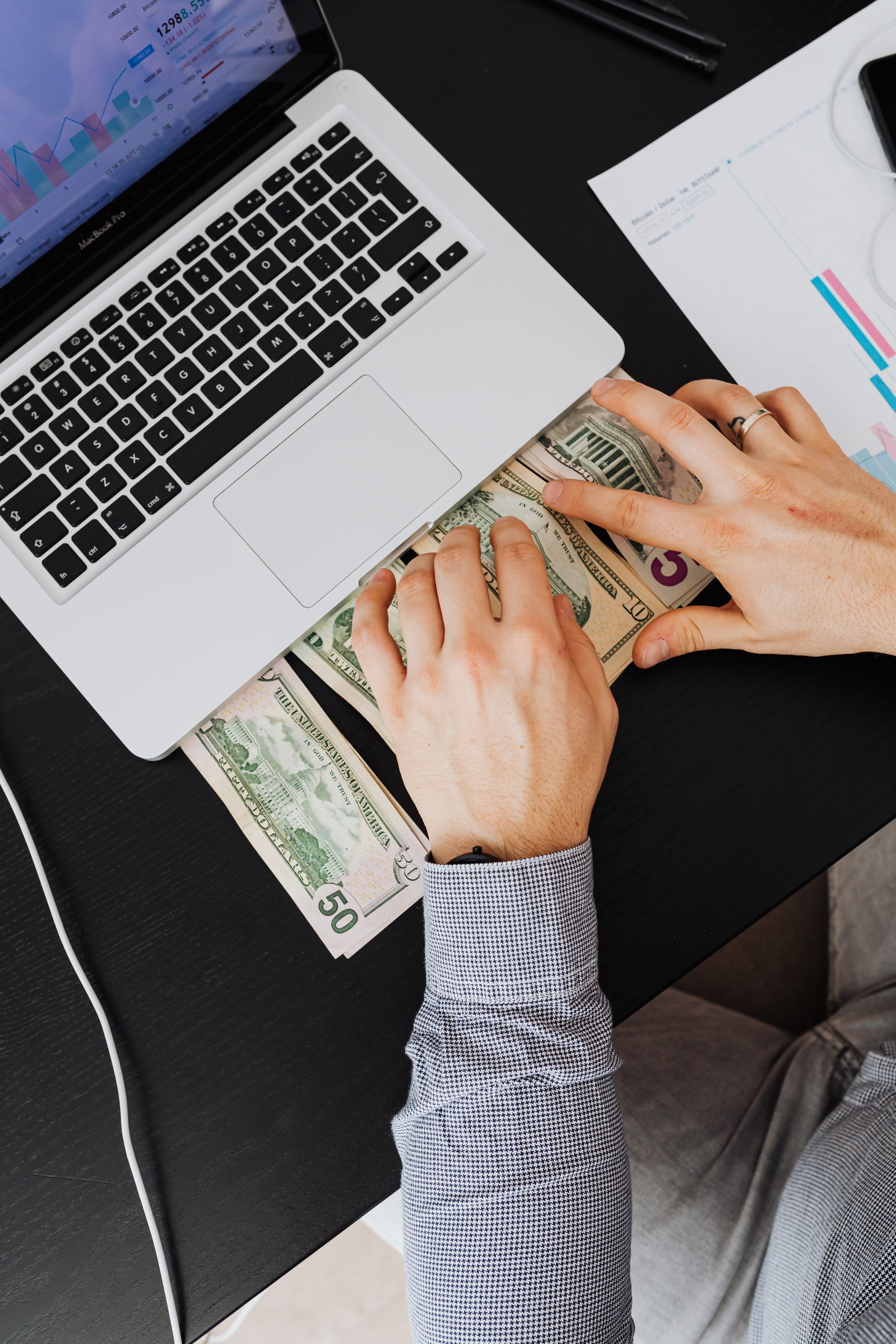 Man counting US dollars at a laptop desk with chart papers, representing financial planning.